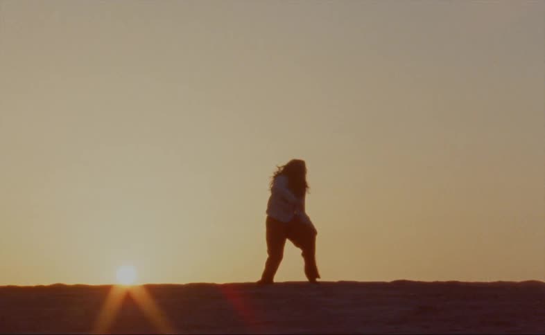 Woman dances outdoors back lit by sun sitting on the horizon