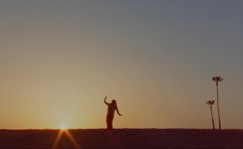 Female dancer dances back lit by light from sun sitting on the horizon