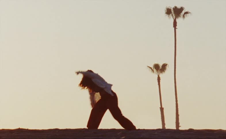 A woman dances alone in a field near palm trees