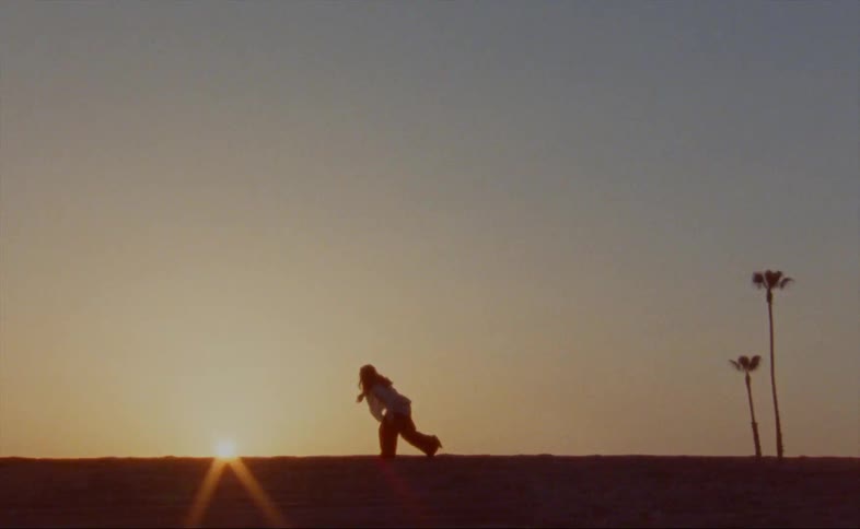 Woman dances on sand silhouetted by setting sun