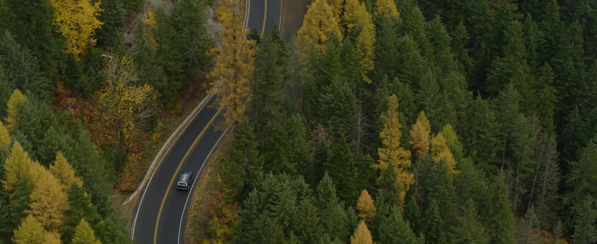 An suv travels on a curving mountain road through forest trees