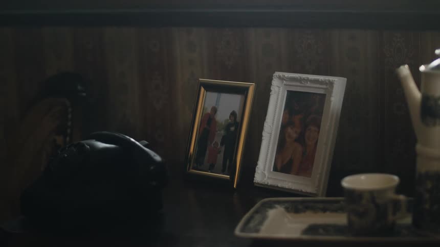 A light from outside flashes across framed photographs on a table