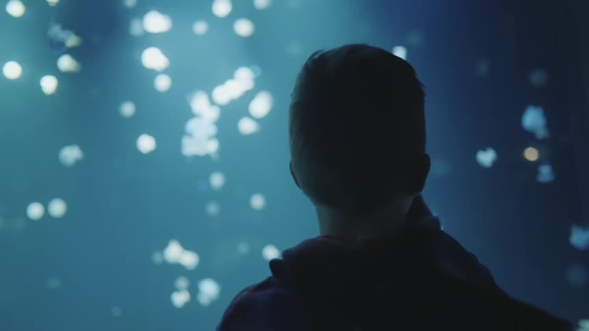 A boy points his finger in a surreal environment with lights floating in a blue atmosphere