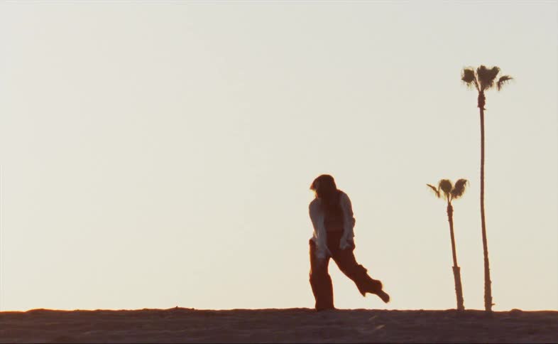 A woman is dancing outdoors while the sun is setting