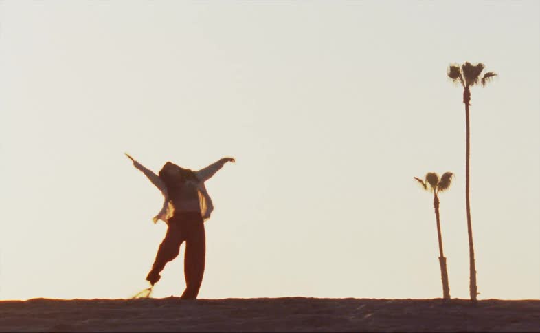 A woman dances in the grass near palm trees