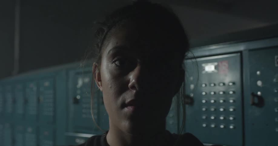 A woman stands staring in a dark locker room