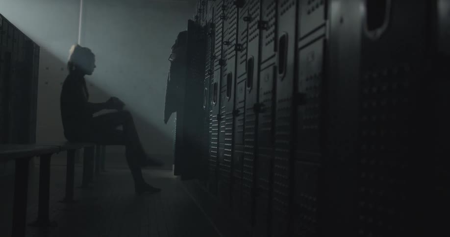 A woman is getting dressed in a dark locker room
