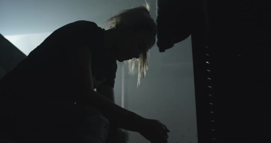 A woman sits on a bench in a dark locker room