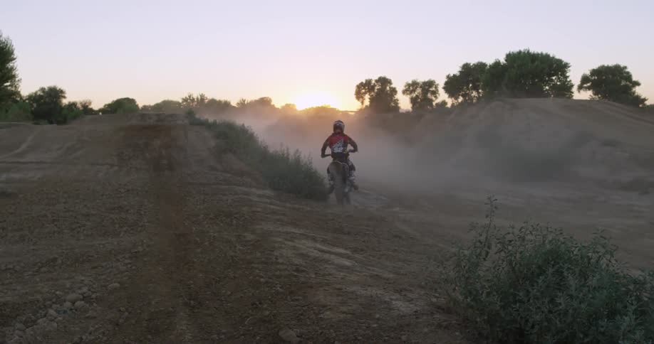 A man is riding his dirt bike down a hilly field
