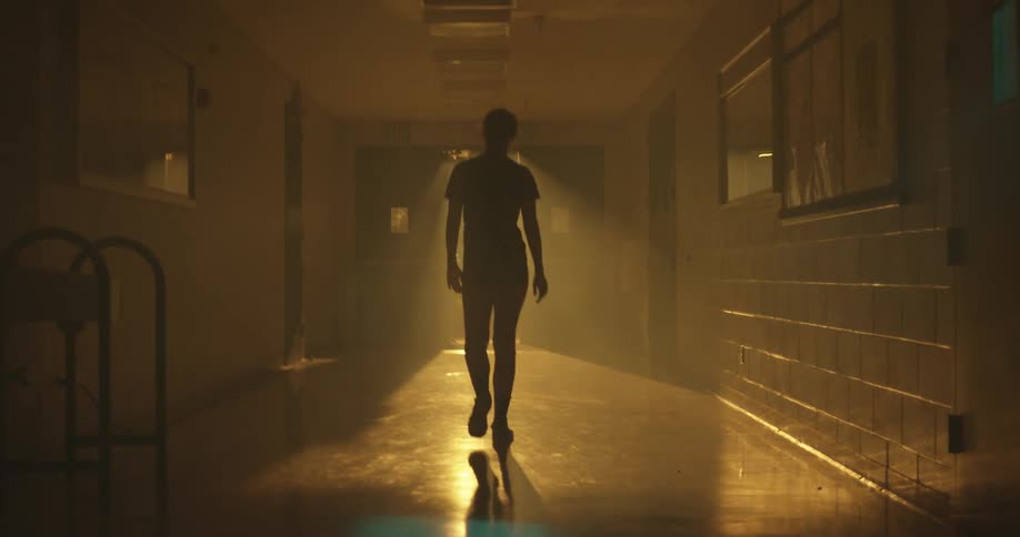 Woman walks through a hallway lit by sunlight at the far end