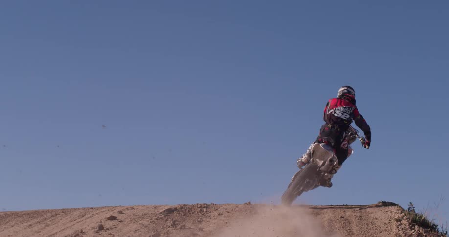 A man rides a dirt bike over a jump while kicking up dust