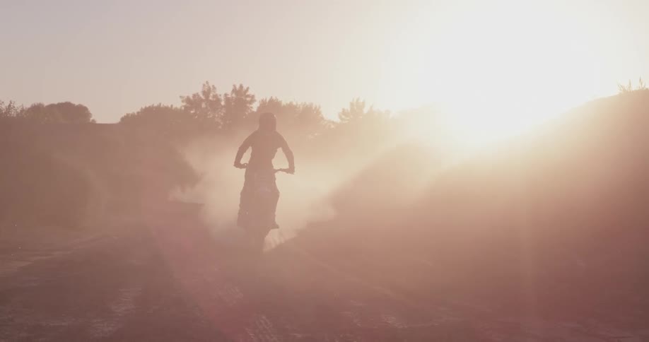 A man rides a dirt bike in a dusty and sunny area