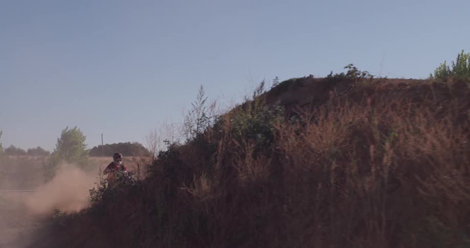 A person rides a dirt bike on a track and off a ramp