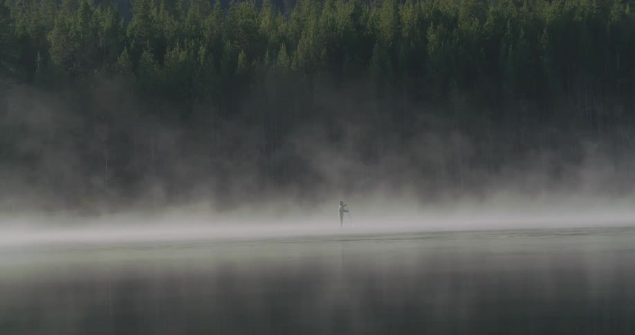 A person paddle boards on a steamy lake