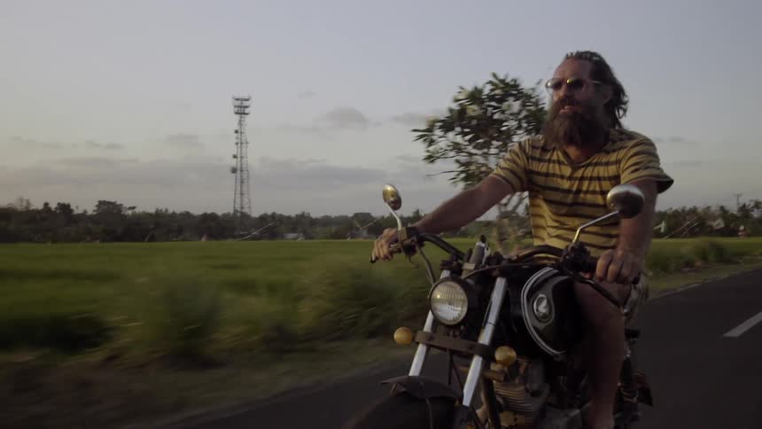 A bearded man driving along a busy rural road