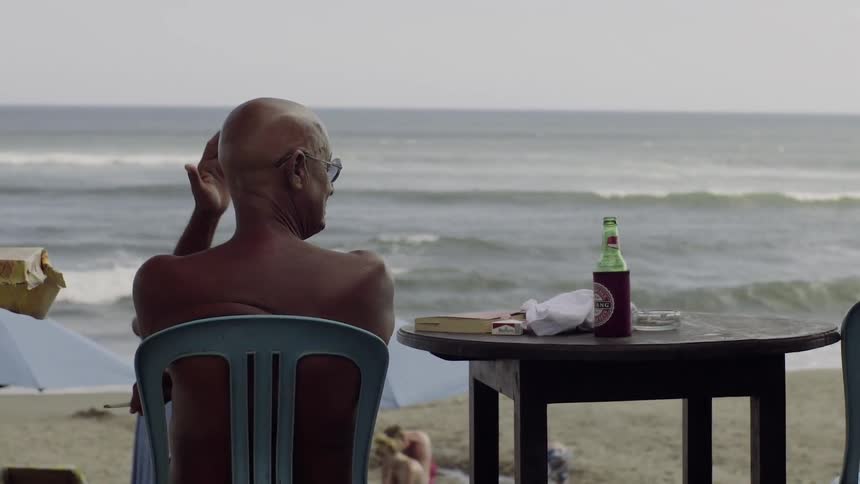 A bald person is sitting in the shade at a beach