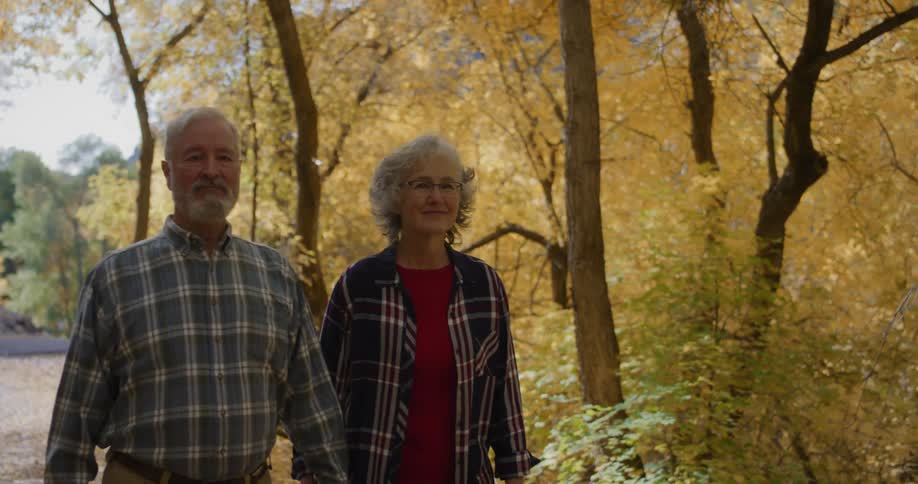 A man and woman hold hands while walking in the woods