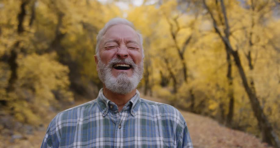 A man standing on a path in a park throws his head back and laughs