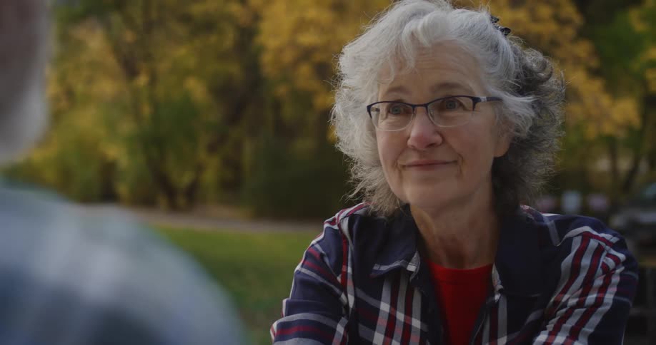 An elderly woman nods while sitting outdoors with an elderly man during the day