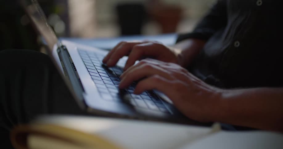 A mans hands are typing on the keyboard of a laptop computer