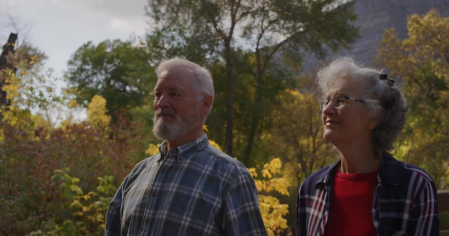 An older couple walking hand in hand smiling as they look at the trees and nature