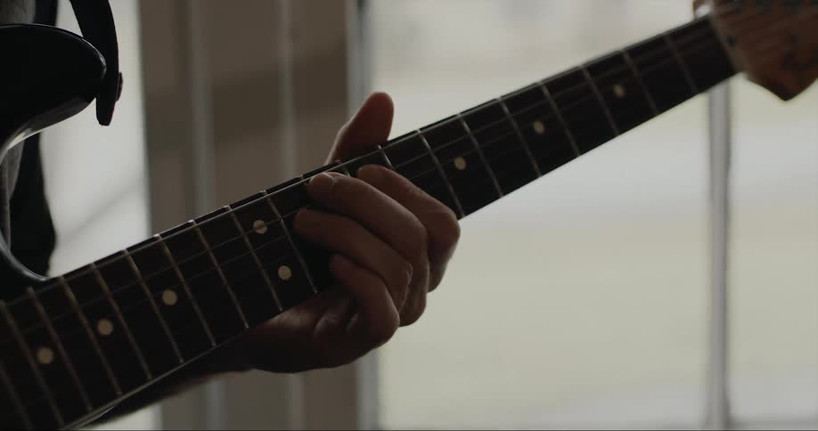 A hand strums the strings on the neck of a guitar