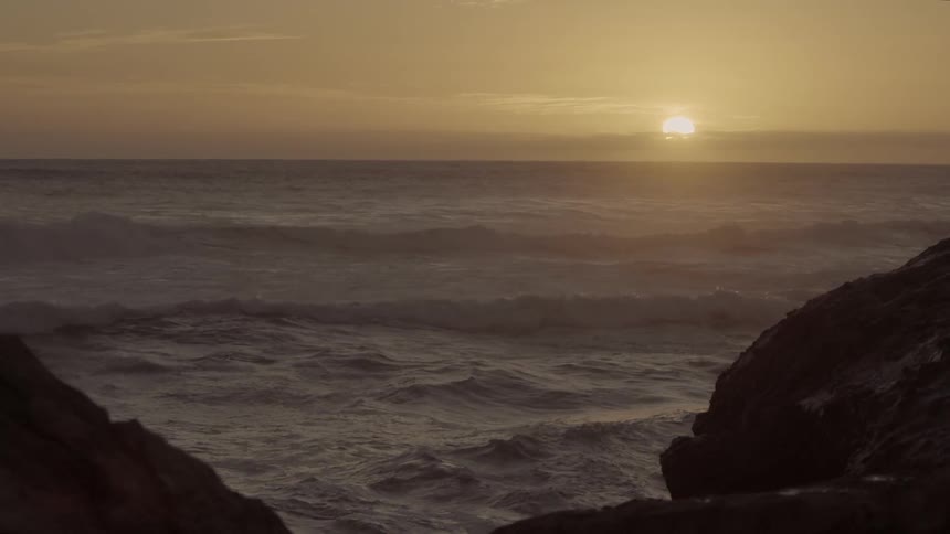 Waves crash on the shore at sunset