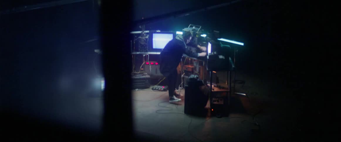 A man is working in a dark room with many televisions and monitors with flashing screens and lights