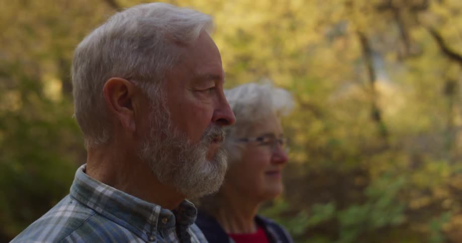 An elderly couple are outside walking among trees with fall colored leaves