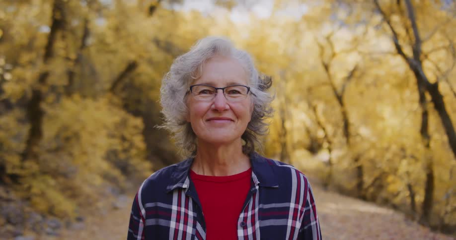 A woman stands and smiles in a forest in the fall