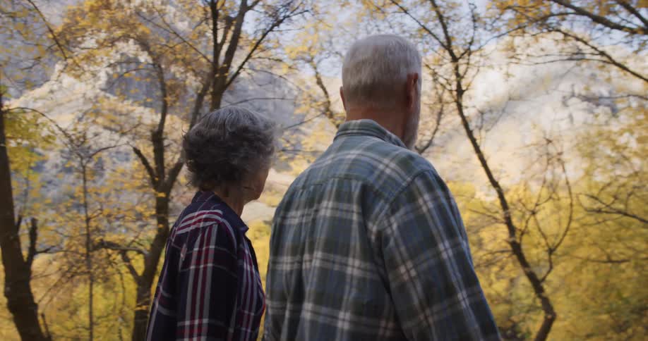 Elderly couple leisurely walking through the trees on a natural park in the mountains