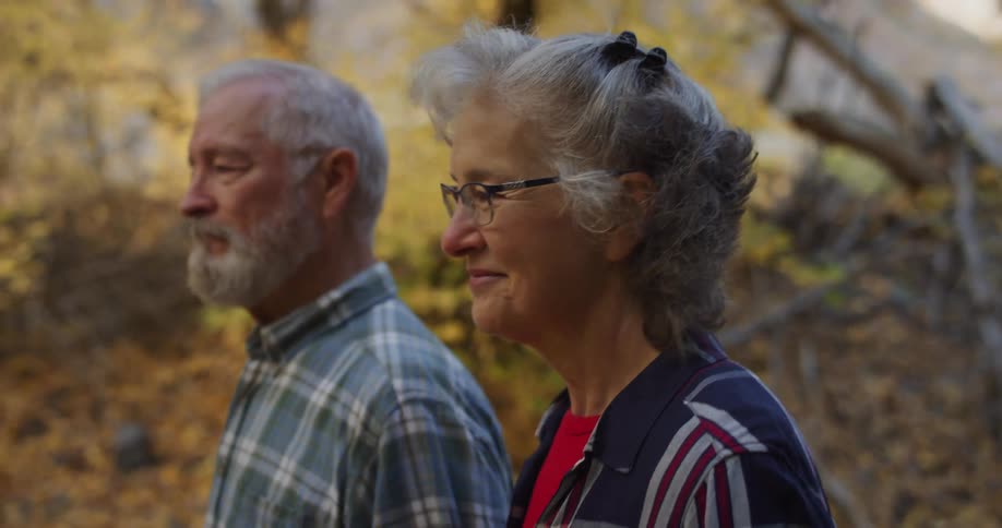A man and woman are smiling and talking as they walk through a forest