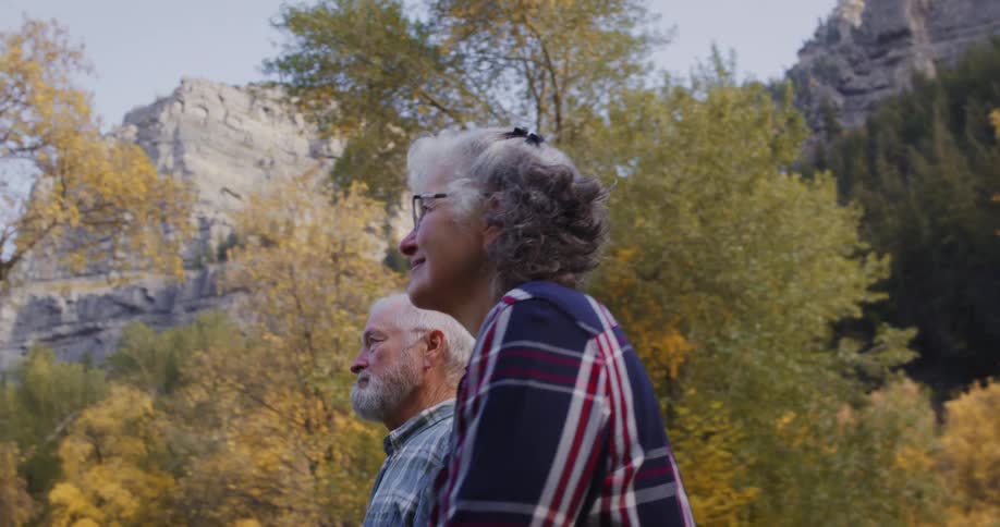 Elderly couple leisurely walking through the trees on a natural park in the mountains