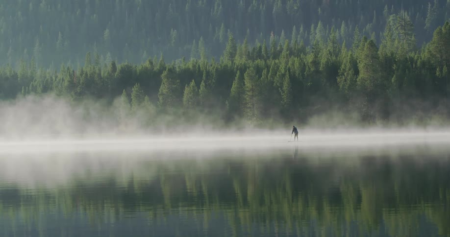 A man is rowing on a board in the water surrounded by fog