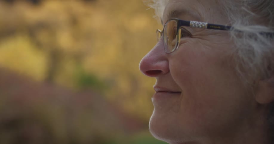 A woman smiles and nods while looking up at trees in the forest