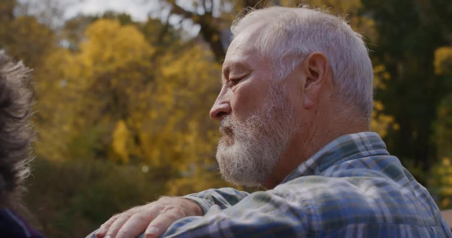 Elderly bearded man reclined on the railing of a bridge looking at a river