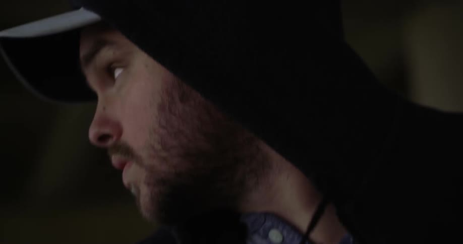 A man wearing a cap and a hoodie gets out of a car