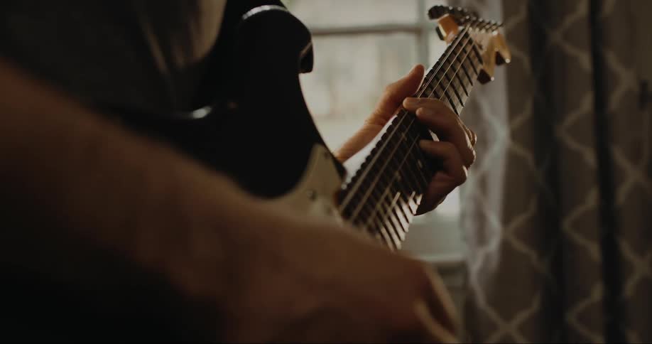 Male guitarist plays electronic guitar in room