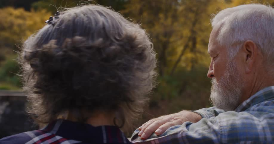 Elderly couple standing on a bridge on a park talk to each other while looking at the nature