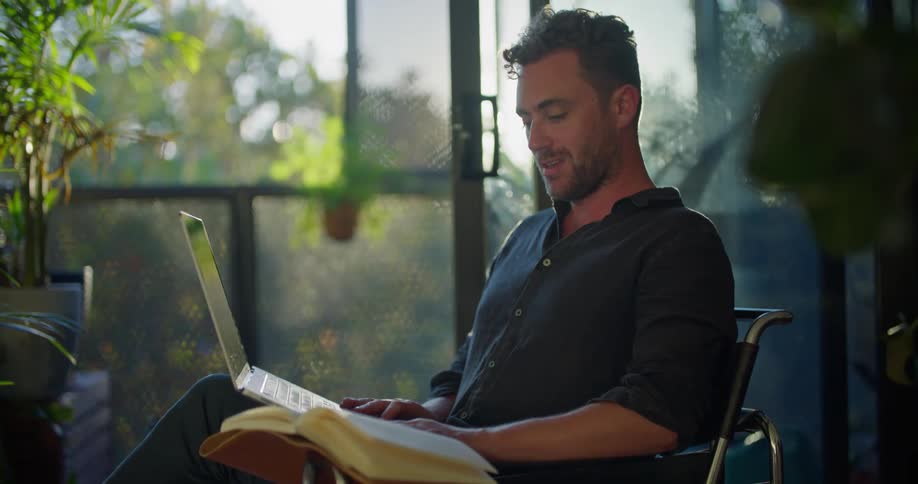 Man sitting on a chair at home working on a laptop talking on a video call at morning