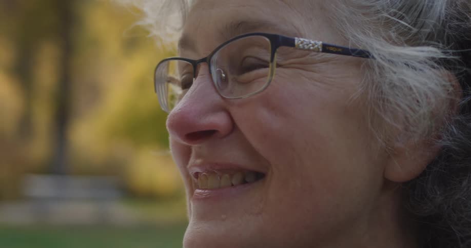 A woman is standing outside on a fall day and talking as she smiles