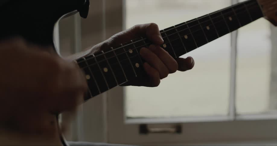 Man strumming an electric guitar on a room at home