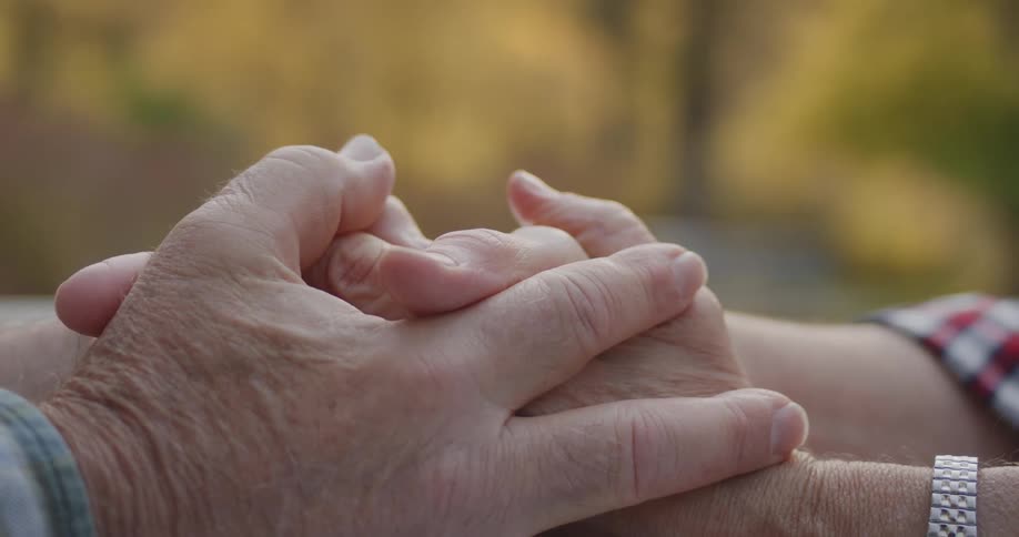 Close up of an elderly couple holding hands over a table outdoors