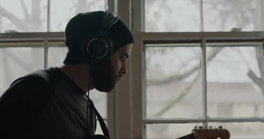 Young man wearing headphones strumming an electric guitar on a room at home
