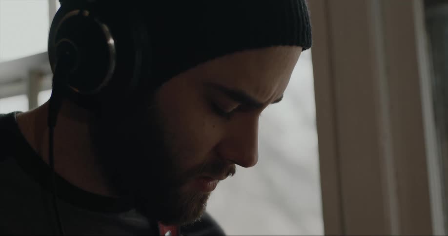 A man is near a window wearing headphones and moving his head to the music