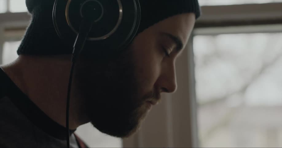 A man is near a window wearing headphones and moving his head to the music