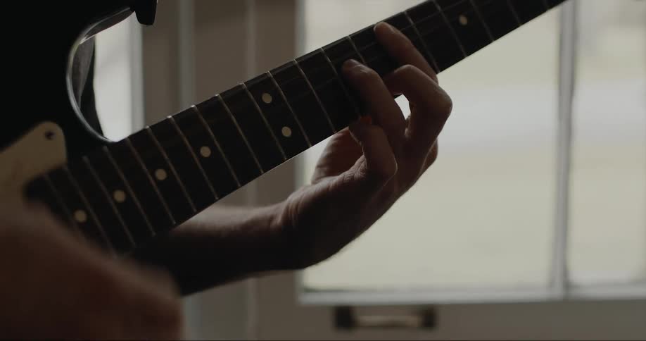 Man strumming an electric guitar on a room at home