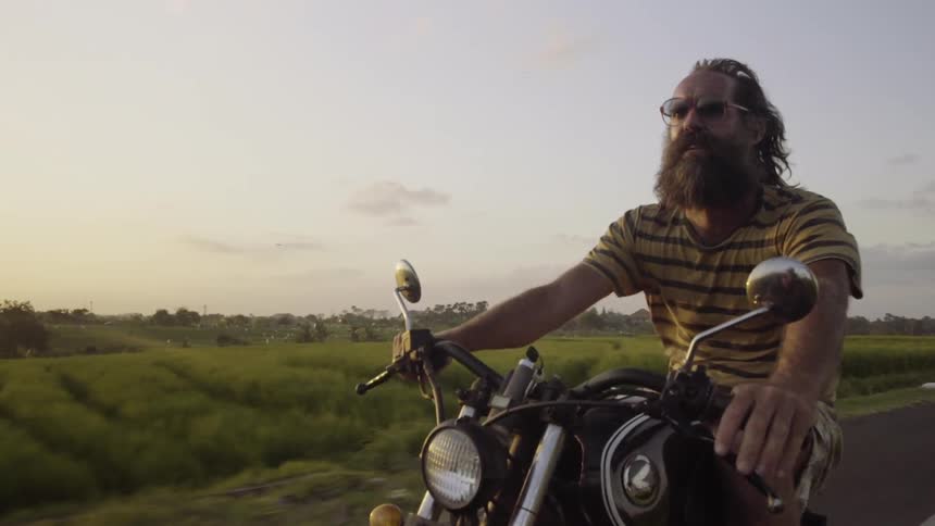 A motorcyclist rides on a rural road at sunset