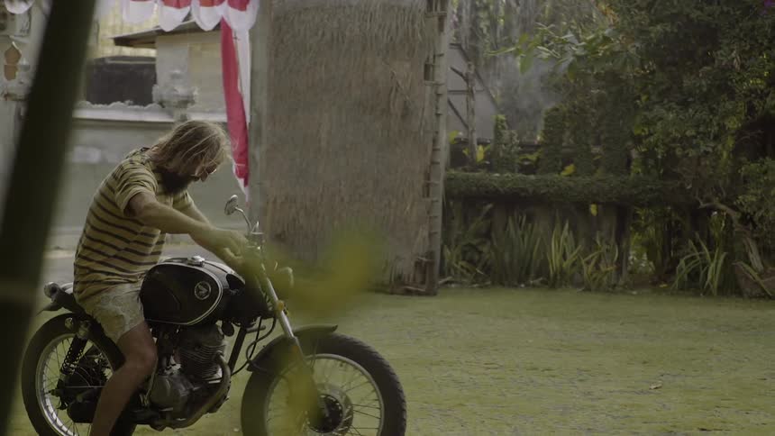 A bearded man gets off his bike and shakes hands with another person