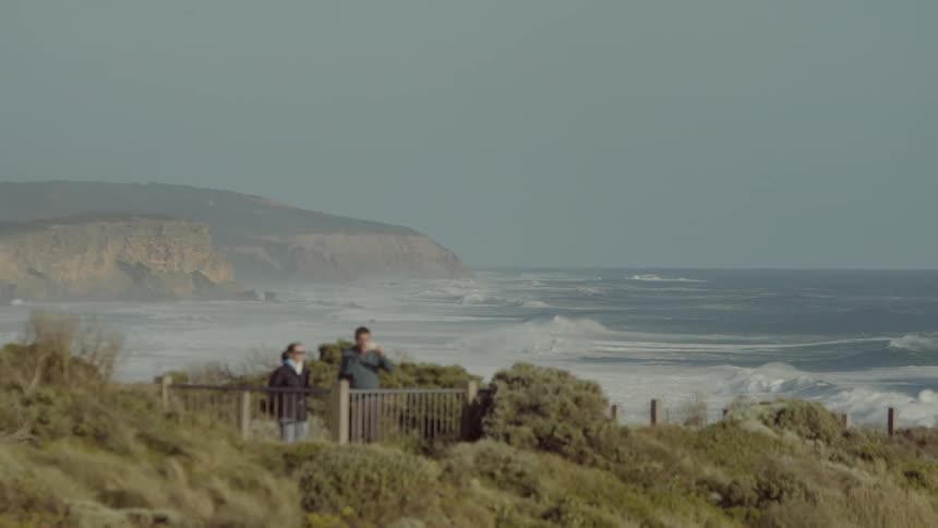 A man and woman go for a walk with the ocean in the background
